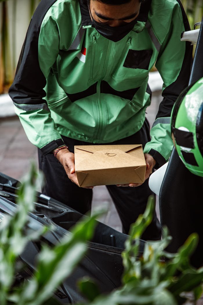 Courier in green uniform holding a package near a scooter